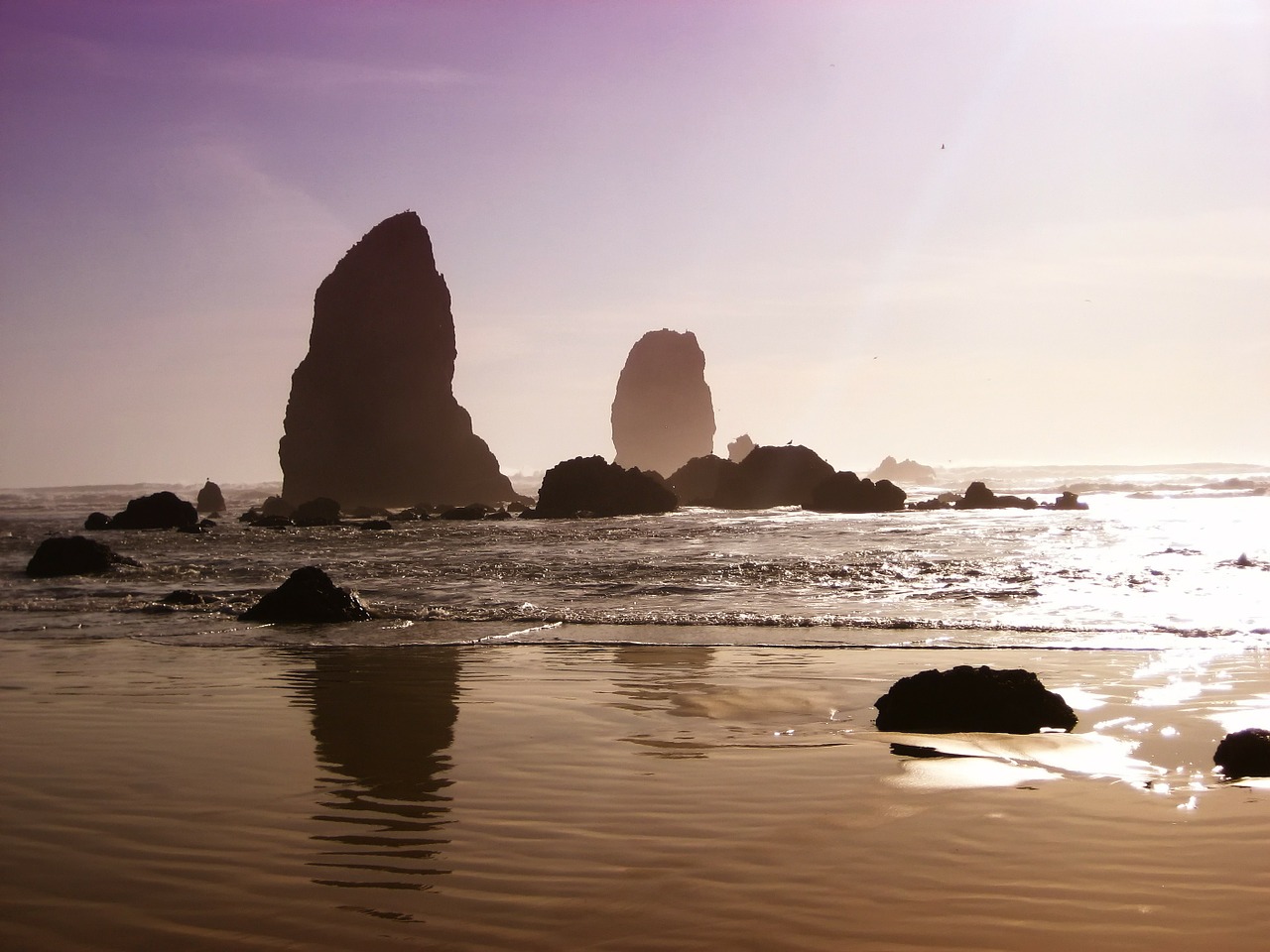 Rocks in the ocean at the Oregon Coast. Tall rocks stand in the water in the distance. Gentle waves roll in.